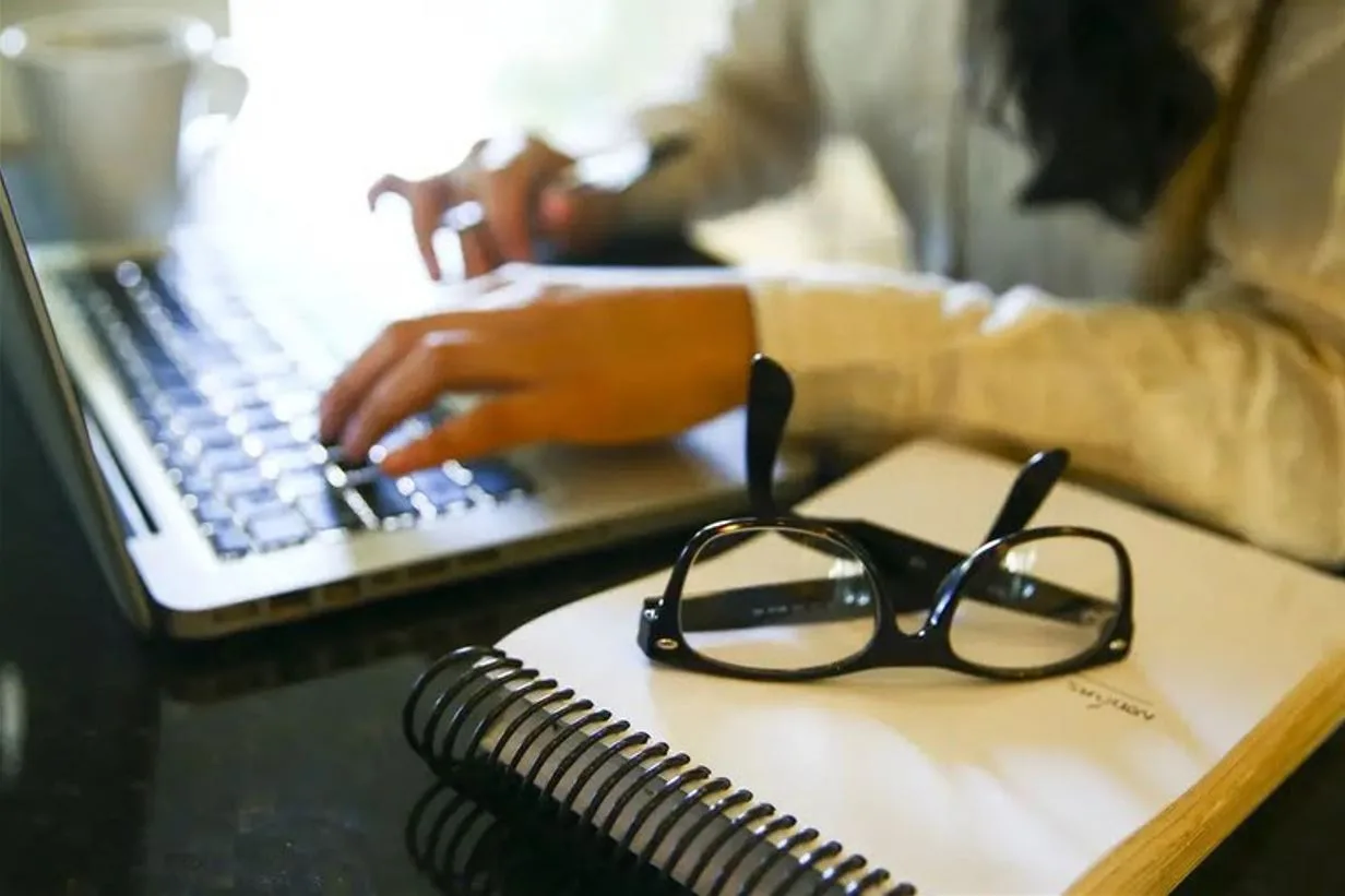 Pessoa usando laptop com óculos e caderno ao lado
