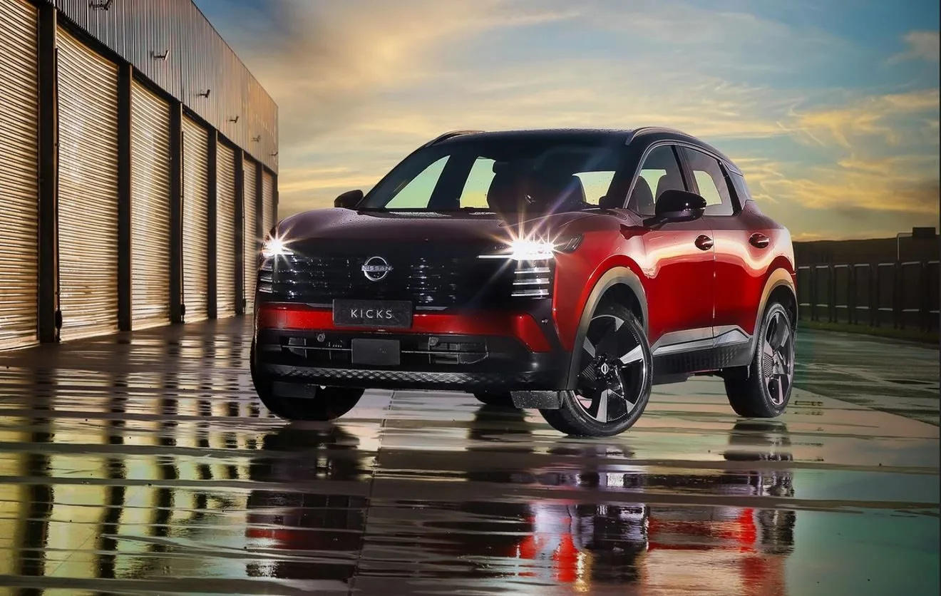 Novo Nissan Kicks 2025 em destaque sob pôr do sol urbano, evidenciando o design renovado com pintura biton em vermelho e teto preto, faróis em LED com assinatura luminosa em filete e rodas de liga leve aro 19", estacionado sobre piso molhado refletindo a iluminação — imagem de divulgação da nova geração do SUV produzido no Brasil.
