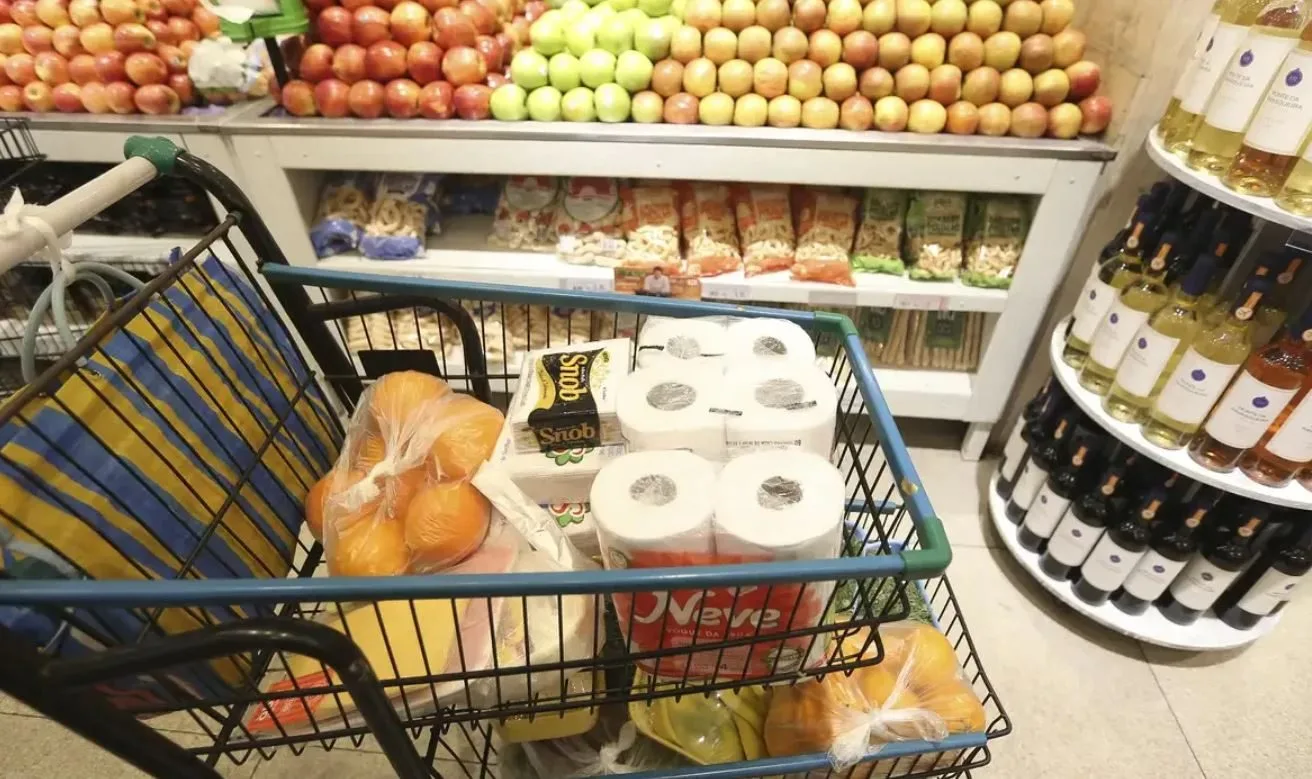 fotofrafia de um carrinho de supermercado, com produtos, como fruta, queijo, presinto, papel higiênico.