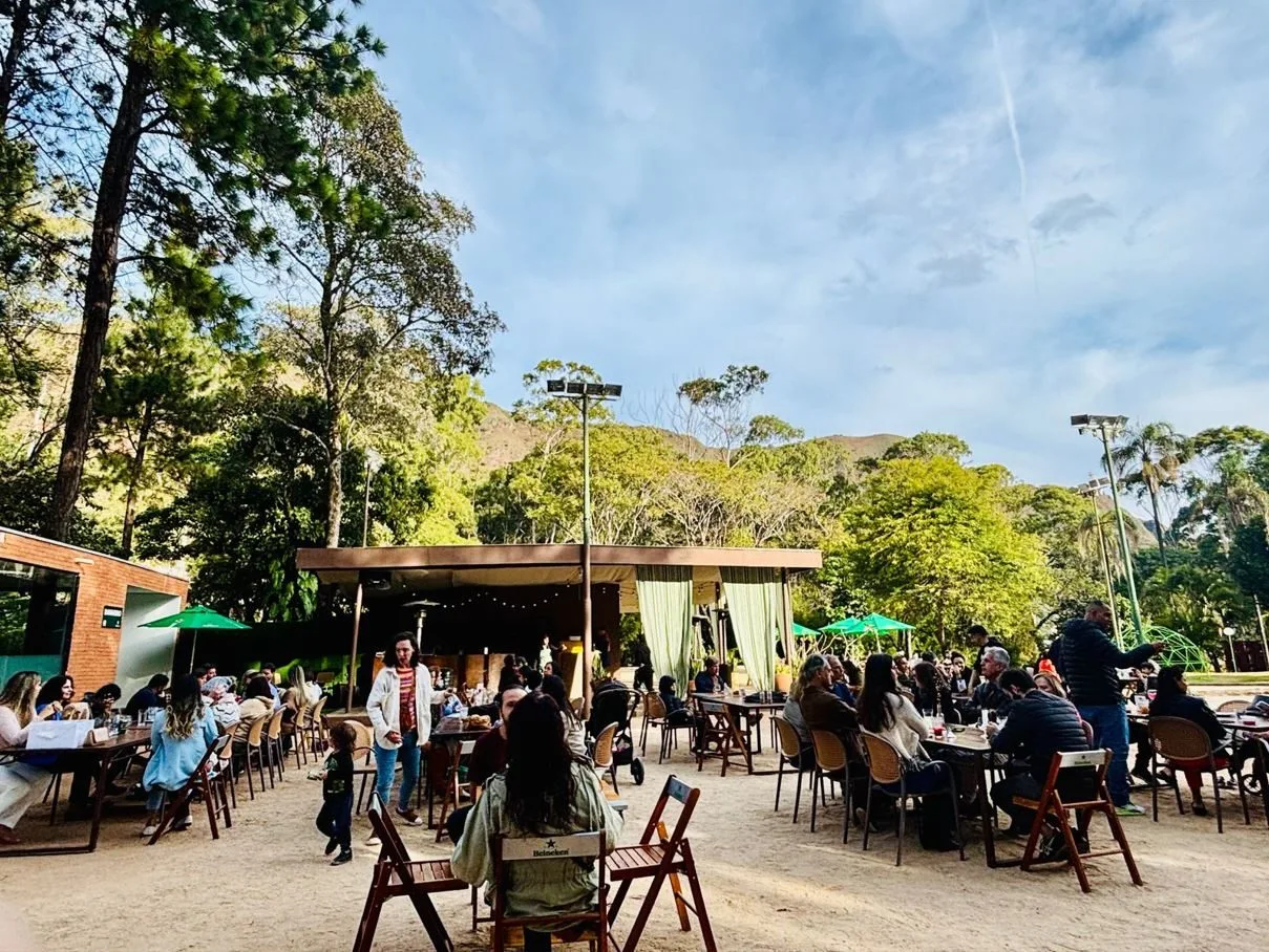 Público aproveita o espaço ao ar livre do Restaurante Botânico no Parque do Palácio, em Belo Horizonte, cercado por vegetação exuberante e montanhas, durante evento de férias infantis com oficinas criativas.