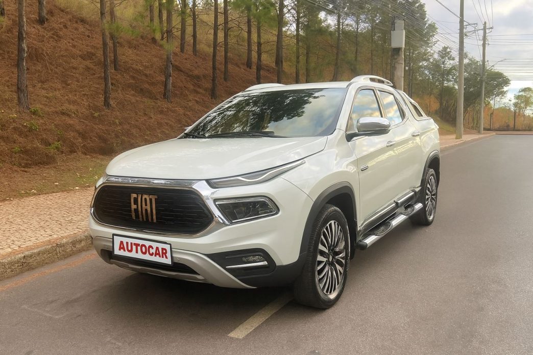 Fiat Toro Ranch 2.2 Turbodiesel na cor branca estacionada à beira de uma rua arborizada. A picape exibe rodas diamantadas, grade frontal com acabamento cromado e faróis full LED, destacando seu design robusto e sofisticado.