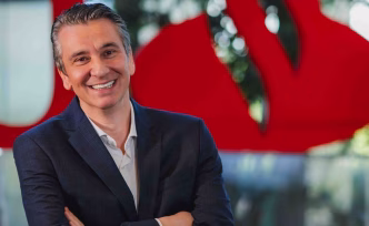 Cezar Janikian, diretor da Financeira do Santander, sorridente, com traje social, diante do logotipo da instituição ao fundo.