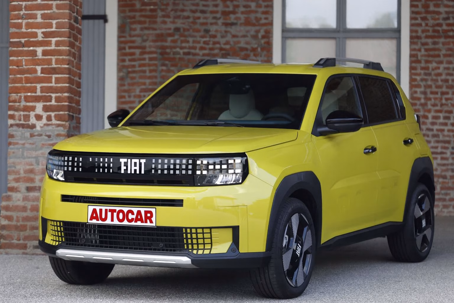 Fiat Grande Panda 2026 em destaque com carroceria amarela vibrante, placa Autocar e fundo com parede de tijolos aparentes.