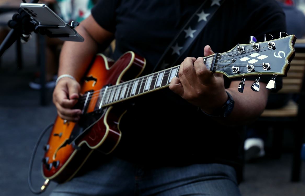 Músico toca guitarra semiacústica durante apresentação ao vivo em evento de rock em espaço ao ar livre, durante o dia.