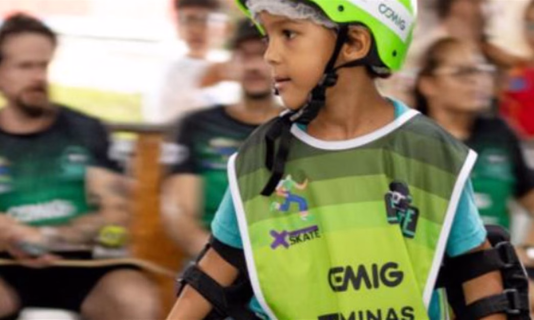 Criança usando capacete verde e colete com logotipo da Cemig participa de atividade esportiva em evento apoiado por projeto social.