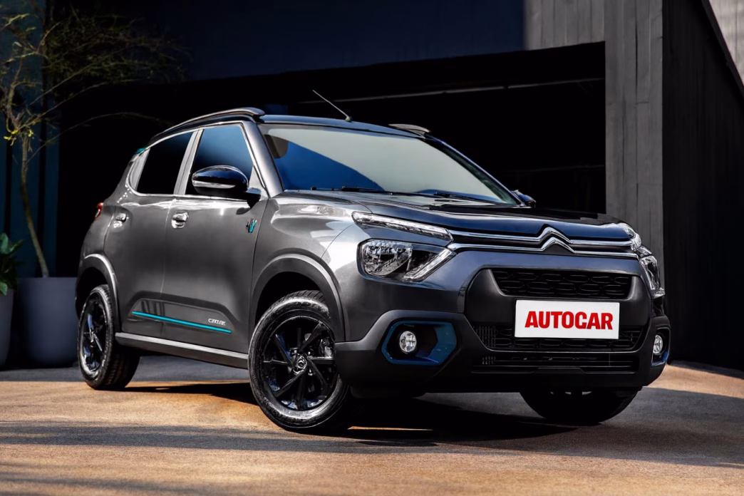 Citroën C3 YOU! 2026 na cor cinza Artense com detalhes azulados, estacionado diante de um prédio moderno, em destaque frontal com a nova placa personalizada AUTOCAR.