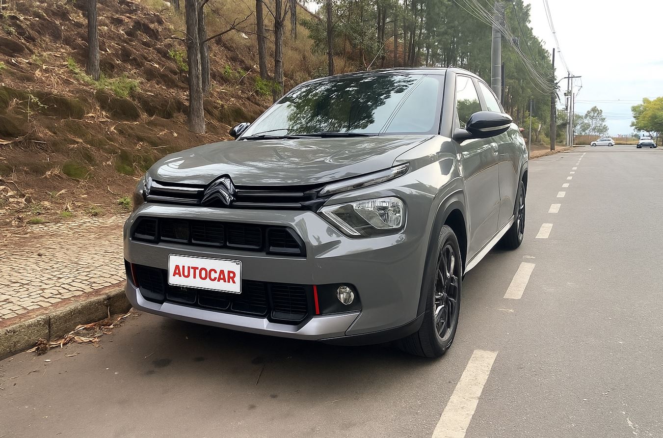 Fotografia do Citroën Basalt Dark Edition T200 estacionado em via urbana ladeada por árvores, destacando o design frontal com faróis afilados, pintura cinza Sting Gray com detalhes escurecidos e rodas pretas de liga leve.