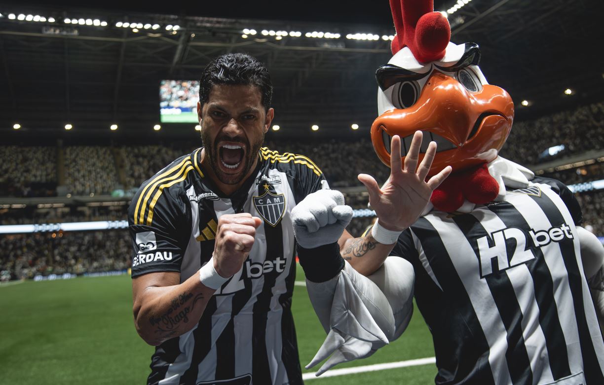 Jogador Hulk, do Atlético Mineiro, comemora intensamente ao lado do mascote Galo Doido, vestindo uniforme preto e branco, na Arena MRV lotada durante a partida contra o Bahia.