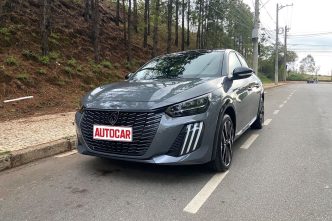 Peugeot 208 GT híbrido 2026 estacionado em rua arborizada, com destaque para o design frontal agressivo, faróis Full LED e grade esportiva.