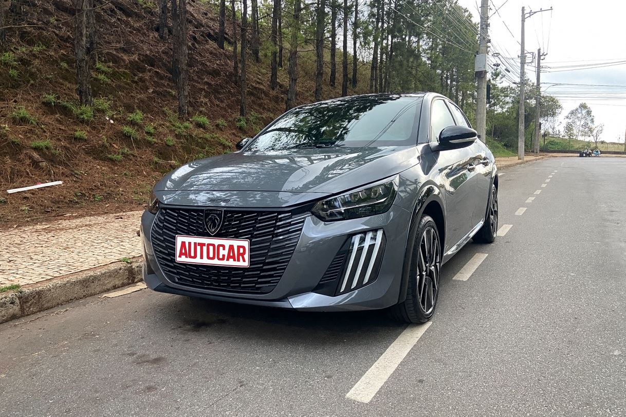 Peugeot 208 GT híbrido 2026 estacionado em rua arborizada, com destaque para o design frontal agressivo, faróis Full LED e grade esportiva.