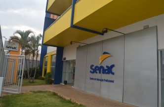 Fachada moderna do Senac Uberlândia, com estrutura em tons de azul e amarelo, jardins bem cuidados e o logotipo da instituição em destaque na entrada principal.