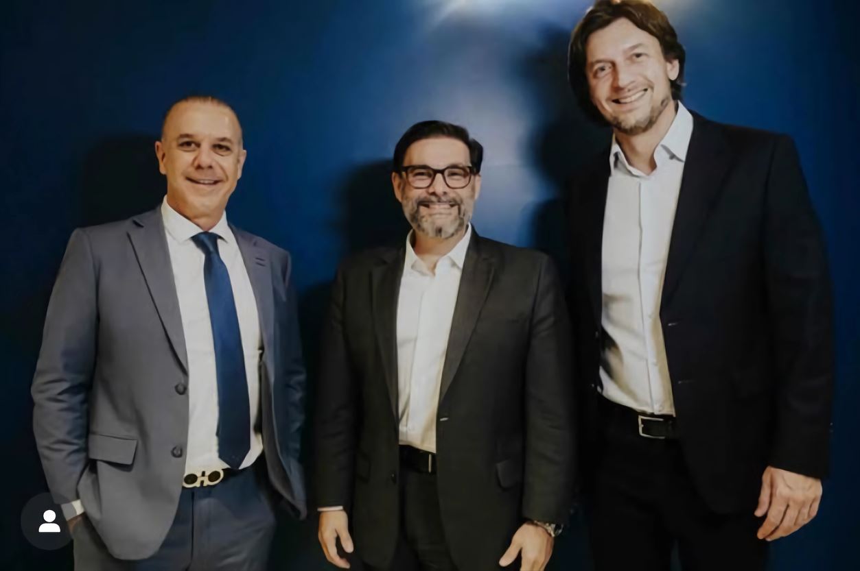 Três homens em trajes sociais posam sorridentes diante de uma parede azul. Eles representam os responsáveis pela nova franquia do Clube de Permuta em São Paulo.