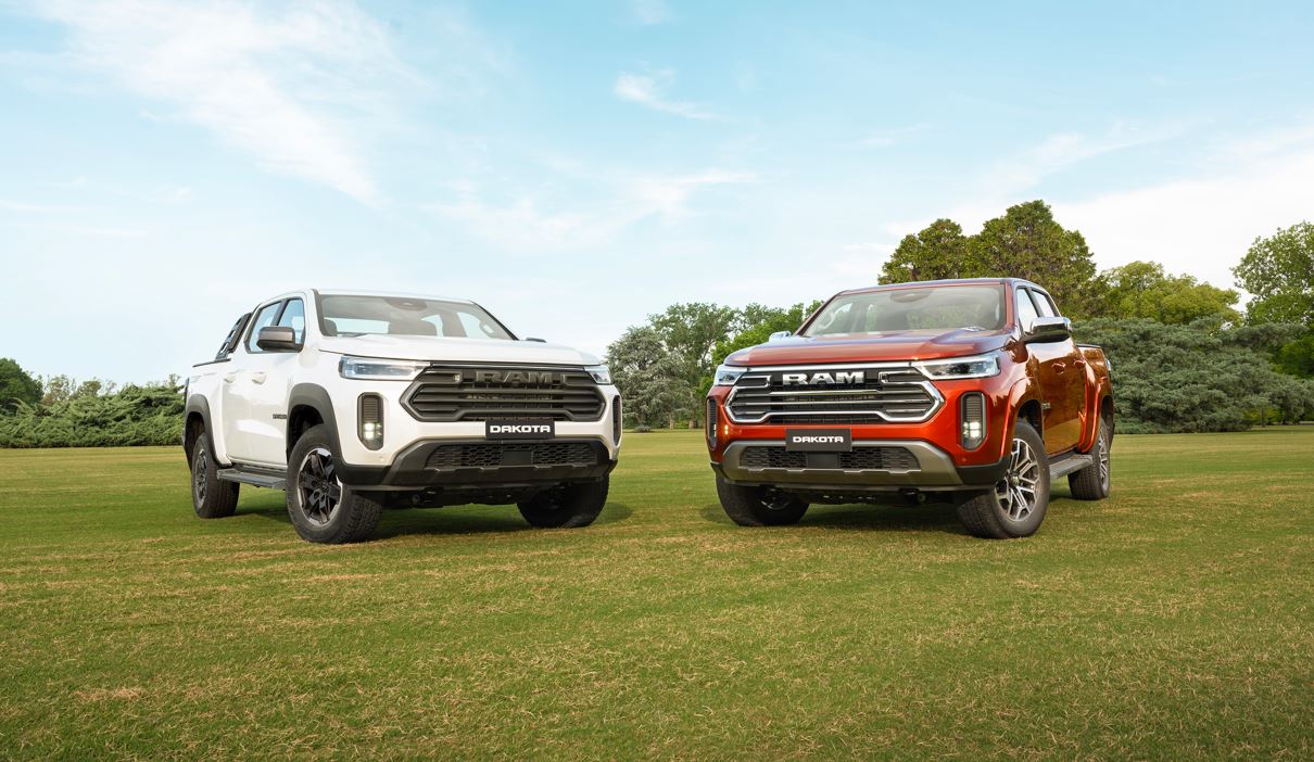 Duas picapes Ram Dakota 2026 estacionadas lado a lado em área verde, exibindo design frontal robusto, grade cromada e assinatura em LED.